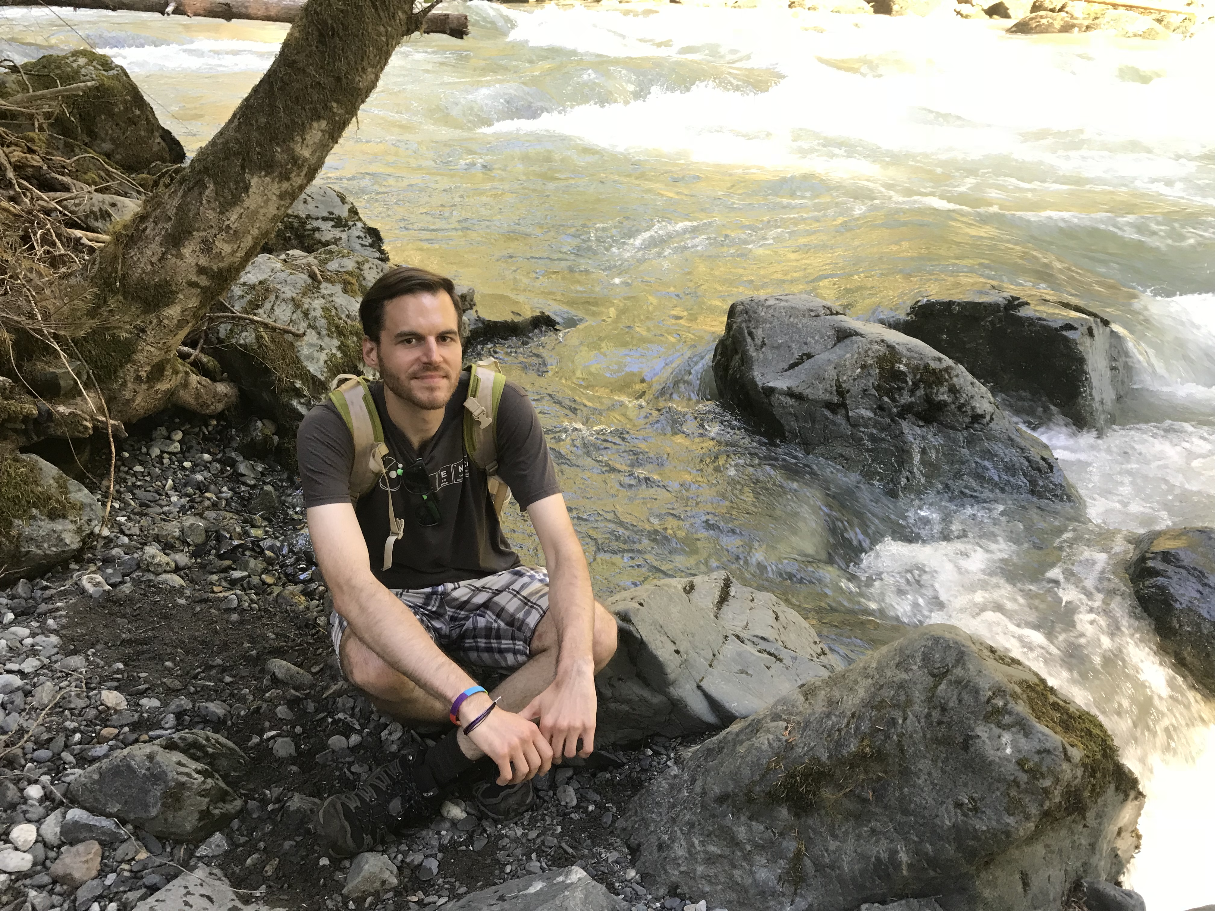 WWU graduate Eric Lawrence crouched by a river with boulders