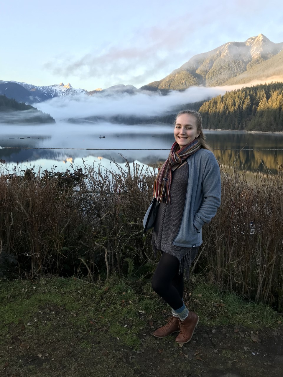  Johanna stands in the middle of a weeded areawith a lake and mountain in the backgroundAnais poses in a field on a cloudy day