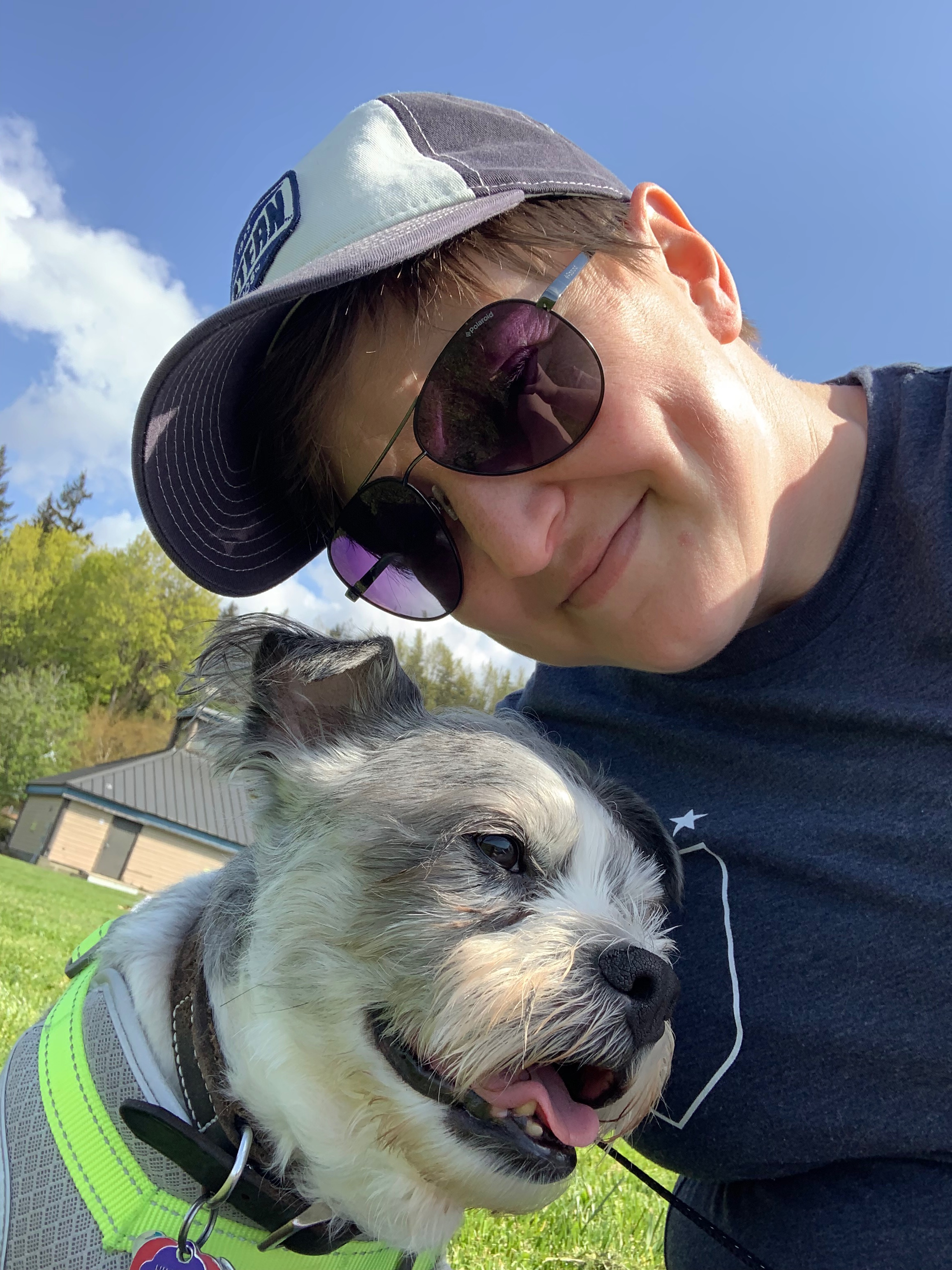 WWU outstanding graduate student Kristina Kelehan with sunglasses and a ball cap on. There's a white and gray dog in the lower left corner named Riley