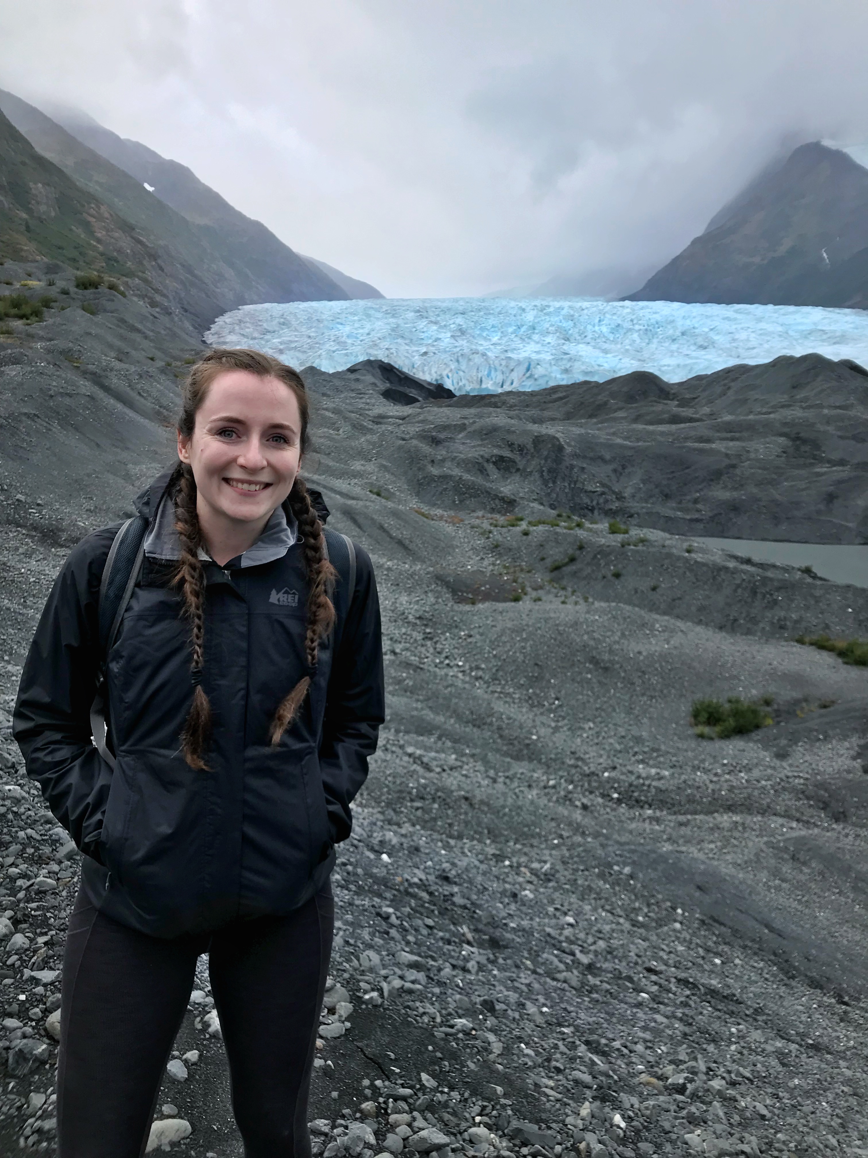 Grad student Gabby Wilson smiling with glacier and misty mountains in the background