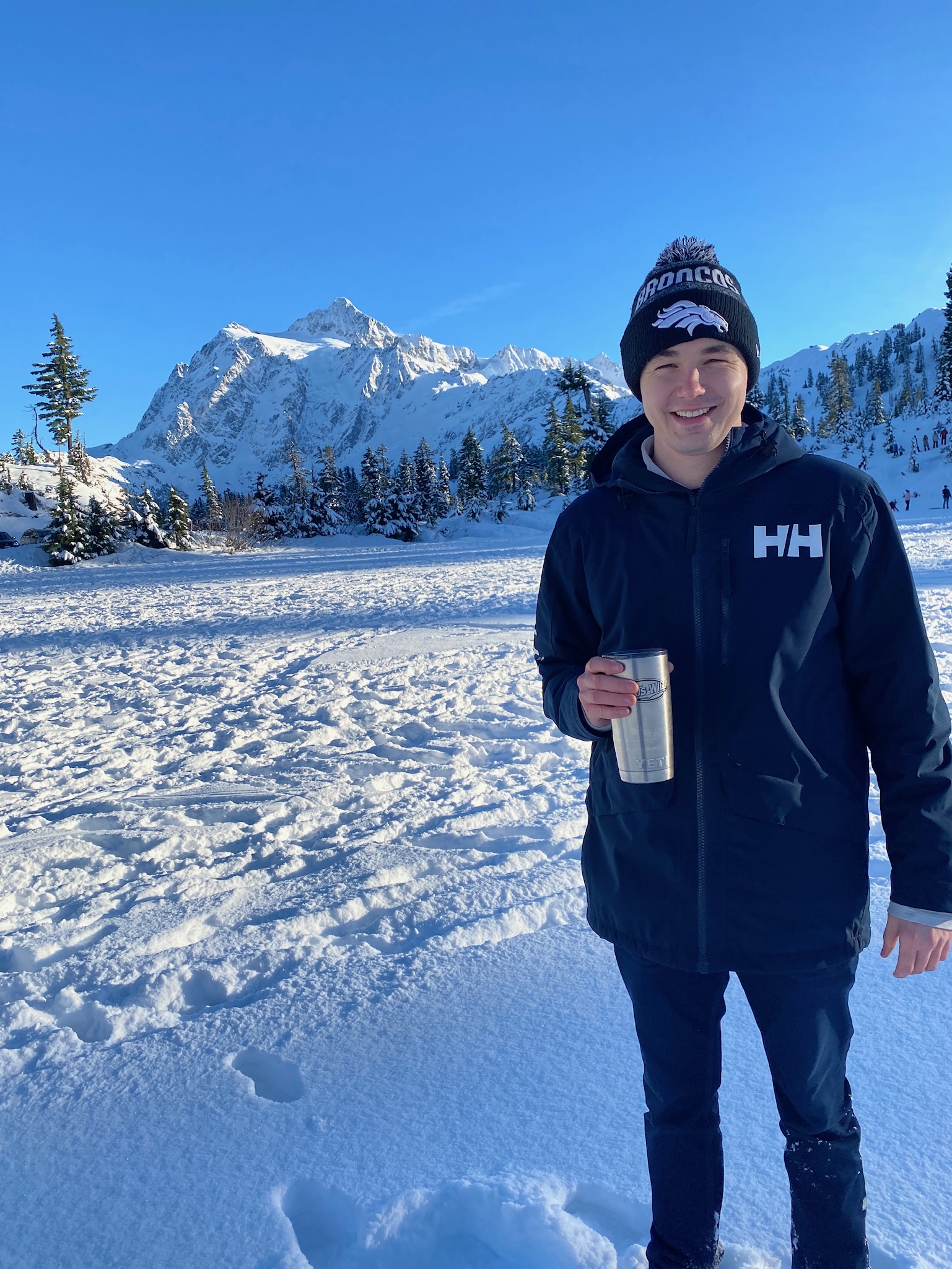 WWU Outstanding Grad Student Taylor Walston holding a travel cup standing in snow with a snowy mountain peak in the backrgound