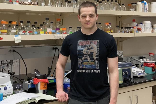 WWU graduate student Heino Hulsey-Vincent standing in lab in front of shelves of instruments