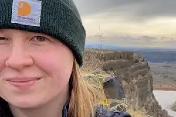 WWU graduate Hannah Fisher smiling with a cliff face and mountain range in the background