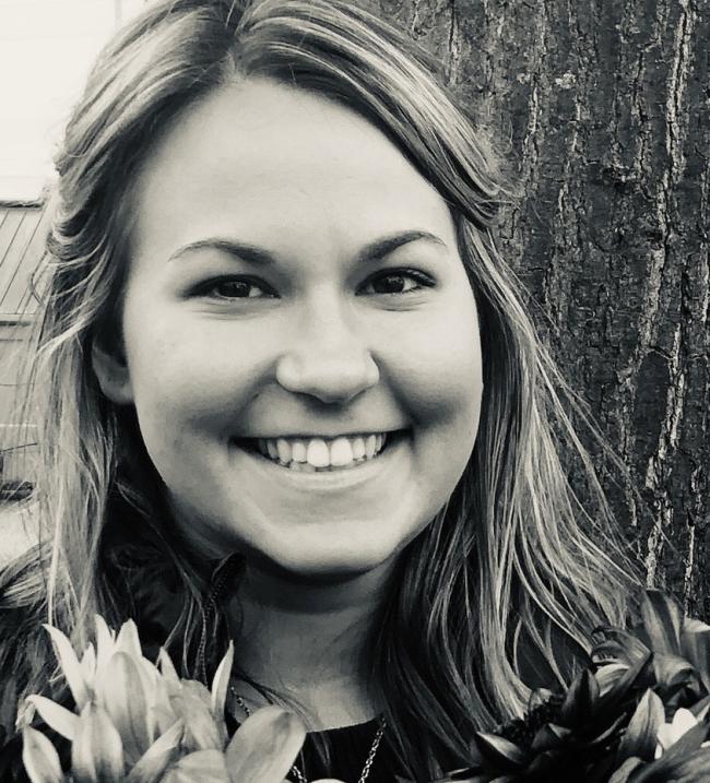 Black and white photo of WWU graduate student Kaitlynn DeMoney holding flowers with tree trunk in the background