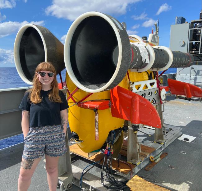 WWU Graduate alum Tessa Beaver standing with hands in pockets aboard a ship next to equipment with two large funnel-shaped cones